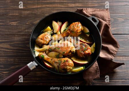 Vista ravvicinata dei bastoncini di pollo cotti con mele ed erbe in padella su tavola di legno. Foto Stock