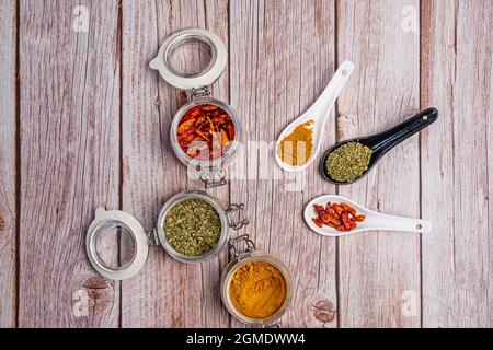 Immagine dall'alto delle spezie all'interno dei vasetti e dei cucchiai di porcellana in bianco e nero su un tavolo di legno Foto Stock