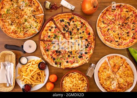 Immagine dall'alto di piatti tipici italiani, pizze assortite a fette, patate, cipolle, posate e pomodori con sale e pepe su tavola di legno Foto Stock