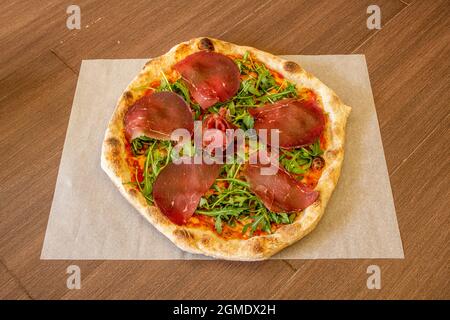 Pizza tirolese con carpaccio, rucola, pomodoro e crosta sottile con bordi tostati Foto Stock