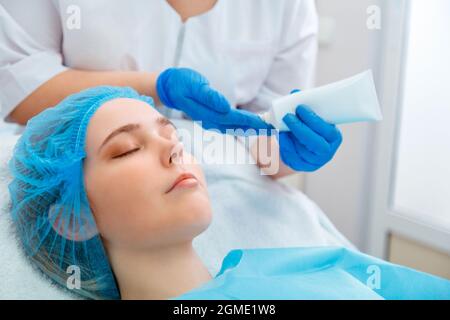 Estetista fare la procedura di bellezza per il cliente della donna. Medico estetista dermatologo applicare crema idratante o crema maschera sulla faccia femminile. Centro benessere cosmetico Foto Stock