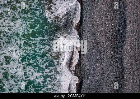 Onde tempestose verdi con schiuma di mare che si infrangono sulla spiaggia di sabbia nera, vista mare texture direttamente sopra Foto Stock