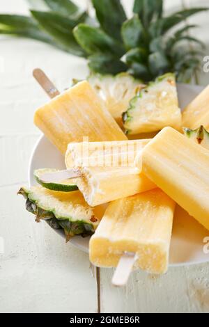 Possicle di ananas al cocco in un cluster su sfondo bianco di legno Foto Stock