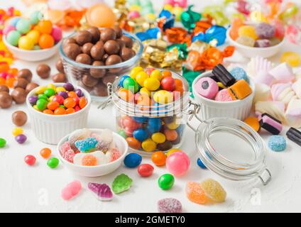 Caramelle al cioccolato al latte in guscio con gomme da zucchero gelate e liquirizia e caramelle di sherbet di frutta su sfondo bianco. Con marshmallow e stra Foto Stock