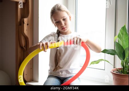 giocattolo in plastica anti-stress sensoriale a tubo pop nelle mani dei bambini. una bambina felice gioca con un giocattolo a fungo a casa. bambini che tengono e giocano Foto Stock