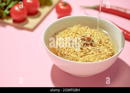 Versando acqua calda in spaghetti istantanei in un recipiente Foto Stock