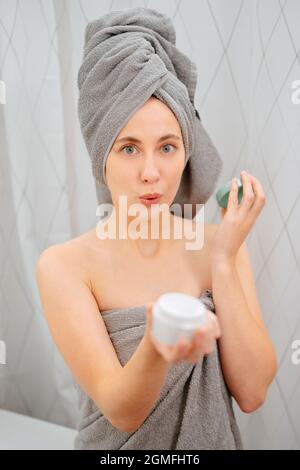 La giovane donna tiene fuori un vaso di crema anti-rughe viso in bagno Foto Stock