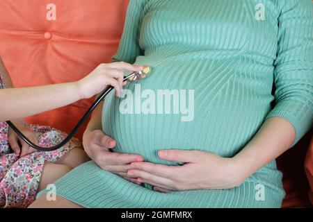 Figlia medico utilizzando uno stetoscopio esaminando bianco donna incinta. Foto Stock