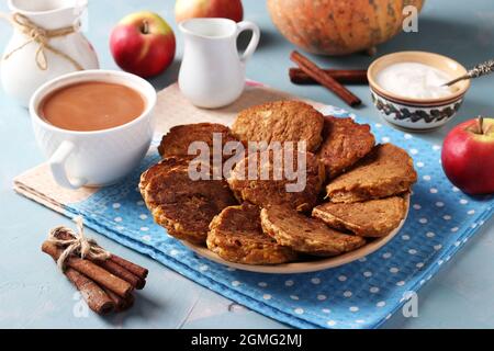 Pancake con zucca e mele per colazione, nonché una tazza di caffè con latte su sfondo azzurro. Foto Stock