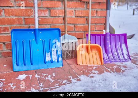 Le pale colorate di plastica della neve si trovano vicino al muro di mattoni del palazzo concetto di famiglia di pulizia della casa e la zona intorno alla casa Foto Stock