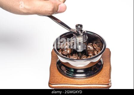 la mano di un uomo tiene la maniglia del macinacaffè per mettere a terra i chicchi di caffè tostati su sfondo bianco Foto Stock