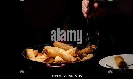 i panini primaverili fritti e profondi si surgono sulla padella su sfondo scuro con la mano, prenderne uno e metterlo in un piccolo piatto Foto Stock