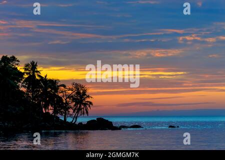 bel crepuscolo colorato blu vimino e arance graduato cielo e mare dietro la silhouette rocciosa riva con alberi di cocco e pietra fotografia con g Foto Stock