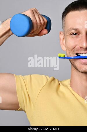 Ritratto di felice uomo adulto sorridente in t-shirt gialla che tiene lo spazzolino in bocca e muto in mano Foto Stock