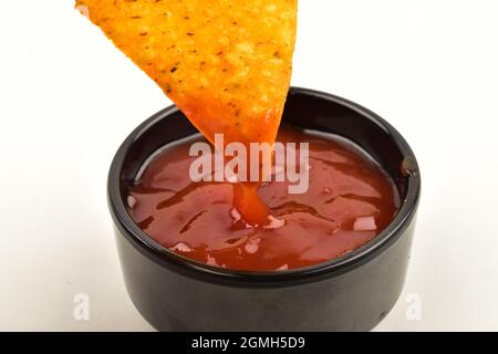 Frammento di Nacho immerso in salsa di pomodoro su sfondo bianco Foto Stock
