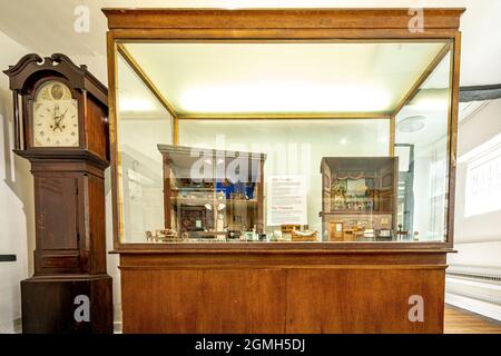 All'interno del Guildford Museum con mostre di storia locale, Surrey, Inghilterra, Regno Unito. Casse di vetro che mostrano vecchie case di bambole, e un orologio di nonno. Foto Stock