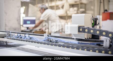 Il tecnico addetto alla fabbrica lavora su una grande taglierina digitale CNC per il taglio del materiale tessile in tessuto Foto Stock