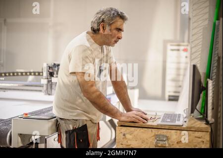 Il tecnico addetto alla fabbrica lavora su una grande taglierina digitale CNC per il taglio del materiale tessile in tessuto Foto Stock