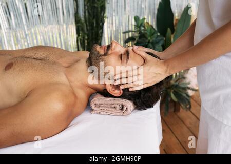 L'uomo rilassato riceve un massaggio alla testa presso il centro benessere. Massaggio anti-stress alla testa, vista laterale Foto Stock