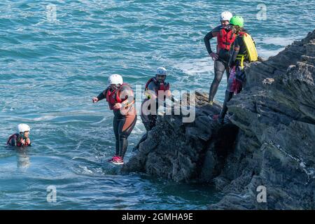 I vacanzieri saltano dalle rocce costellando con una guida su Towan Head a Newquay in Cornovaglia. Foto Stock