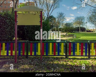 Cartello vuoto all'ingresso di un parco giochi in città, con un'area di riposo con panchine ed edifici sullo sfondo Foto Stock