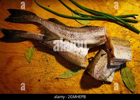 Pezzi freschi di pesce con cipolle verdi e spezie su un tavolo di legno Foto Stock