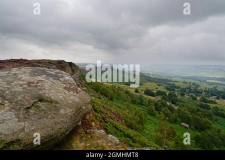 Le nuvole grigie si estendono dalle rocce ricoperte di lichen di Curbar Edge nel Derbyshire Peak District fino a una valle lontana avvolta dalla nebbia. Foto Stock