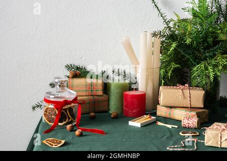 Tavolo natalizio o di Capodanno decorato per le feste, rametti di thuja e abete rosso, nocciole e fette di agrumi secchi, candele e confezioni regalo Foto Stock