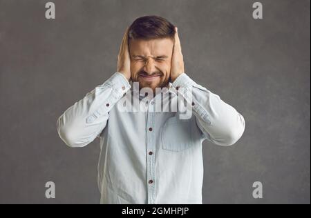 L'uomo stressato e frustrato con occhi chiusi e orecchie coperte dalle mani squints Foto Stock