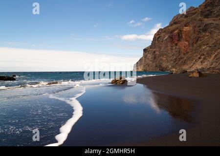 Una spiaggia di sabbia nera sull'oceano atlantico a la Gomera, una delle isole canarie. Il cielo è morramato nella sabbia bagnata. Foto Stock