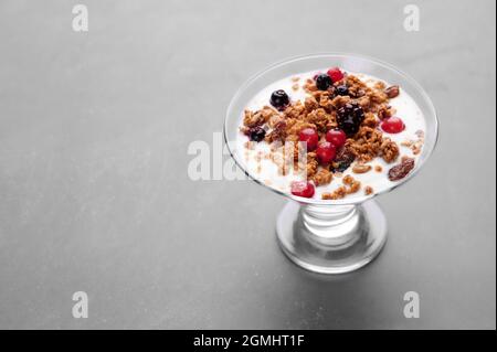 Tazza di yogurt fresco con cereali e frutta su sfondo grigio Foto Stock