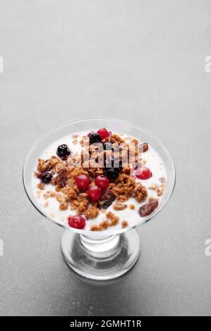 Tazza di yogurt fresco con cereali e frutta su sfondo grigio Foto Stock
