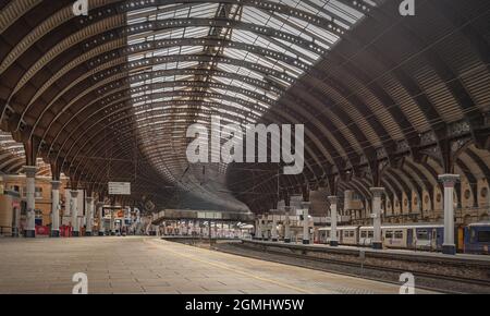 Un panorama di un atrio della stazione ferroviaria. Una tettoia di ferro del XVIII secolo si curva sopra le piattaforme e la luce del sole cade sulla piattaforma. Una footbrid Foto Stock