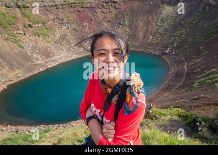 Asian lady in maglietta rossa nella parte anteriore di un color turchese del lago del cratere in Islanda Foto Stock