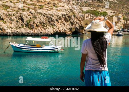 Una donna asiatica si gode della vista sulle acque della Baia di Xlendi a Gozo Isola, parte dell'archipel maltese Foto Stock