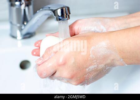 La giovane donna caucasica lava le mani con acqua e sapone in bagno. Foto Stock