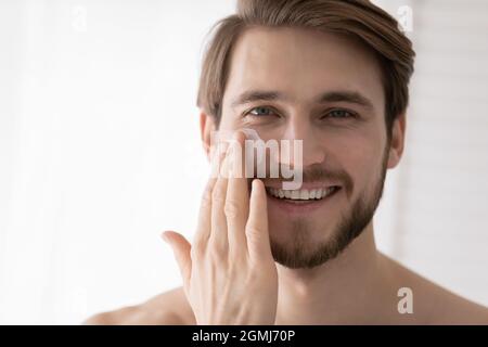 Primo piano ritratto bel uomo applicare crema viso Foto Stock