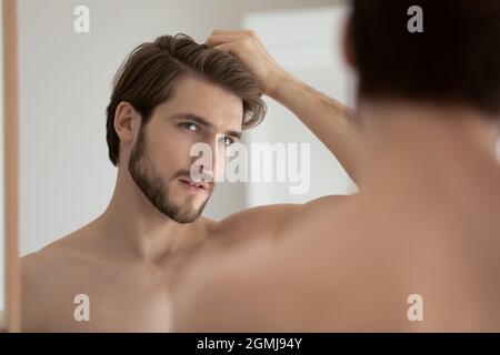 L'uomo osserva nei capelli di tocco dello specchio ritiene interessati dovuto receding Foto Stock