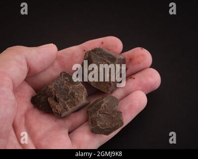 Un uomo che tiene in mano pezzi di cioccolato fondente. Tasto basso. Primo piano. Foto Stock