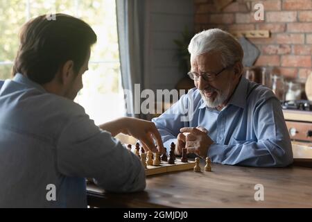 Uomo maturo sorridente con figlio grownup che gioca a scacchi insieme Foto Stock