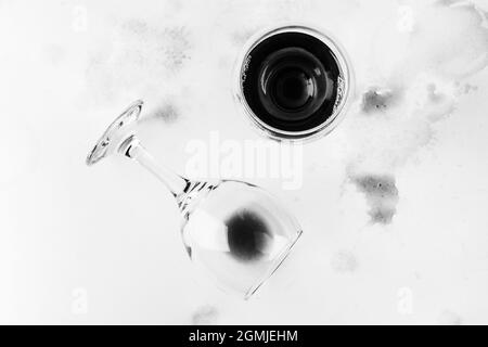 un bicchiere di vino rosso e un bicchiere rovesciato con i resti di vino su uno sfondo bianco adrenato e macchiato con vista dall'alto del vino, foto bianco nero Foto Stock