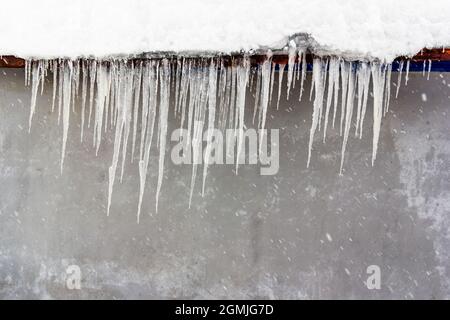 ghiaccioli appesi al tetto contro il wal grigio Foto Stock