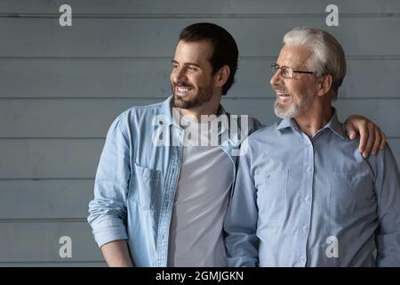 Felice due generazioni di uomini abbracciando, guardando a distanza Foto Stock