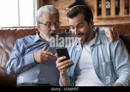 Overjoyed sorprende due generazioni di uomini che guardavano lo schermo del telefono Foto Stock