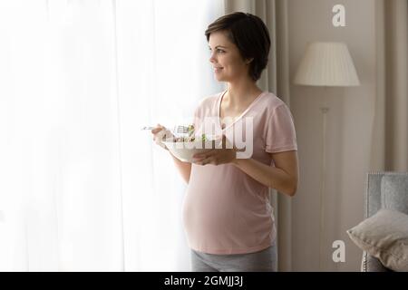 Felice giovane donna incinta mangiare vitamina insalata gustare verdure fresche Foto Stock