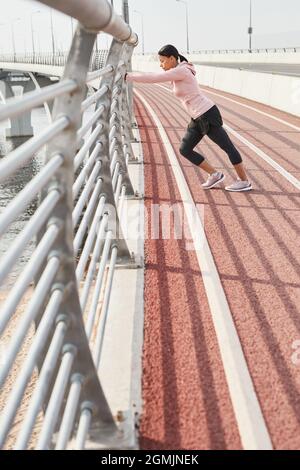 Giovane donna in abbigliamento sportivo appoggiata sulla ringhiera facendo esercizi sullo stadio Foto Stock