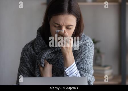 Primo piano su donna malsana avvolto in plaid soffiare naso corrente Foto Stock