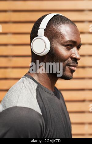 Giovane africano in cuffie senza fili godere della musica mentre si trova all'aperto Foto Stock