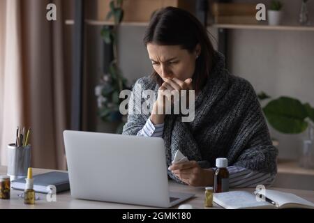 Donna d'affari malsana avvolta in plaid che lavora sul laptop a casa Foto Stock