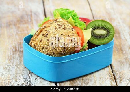 Scatola per il pranzo sana contenente un rotolo di formaggio a grani interi con lattuga, pomodoro e kiwi Foto Stock